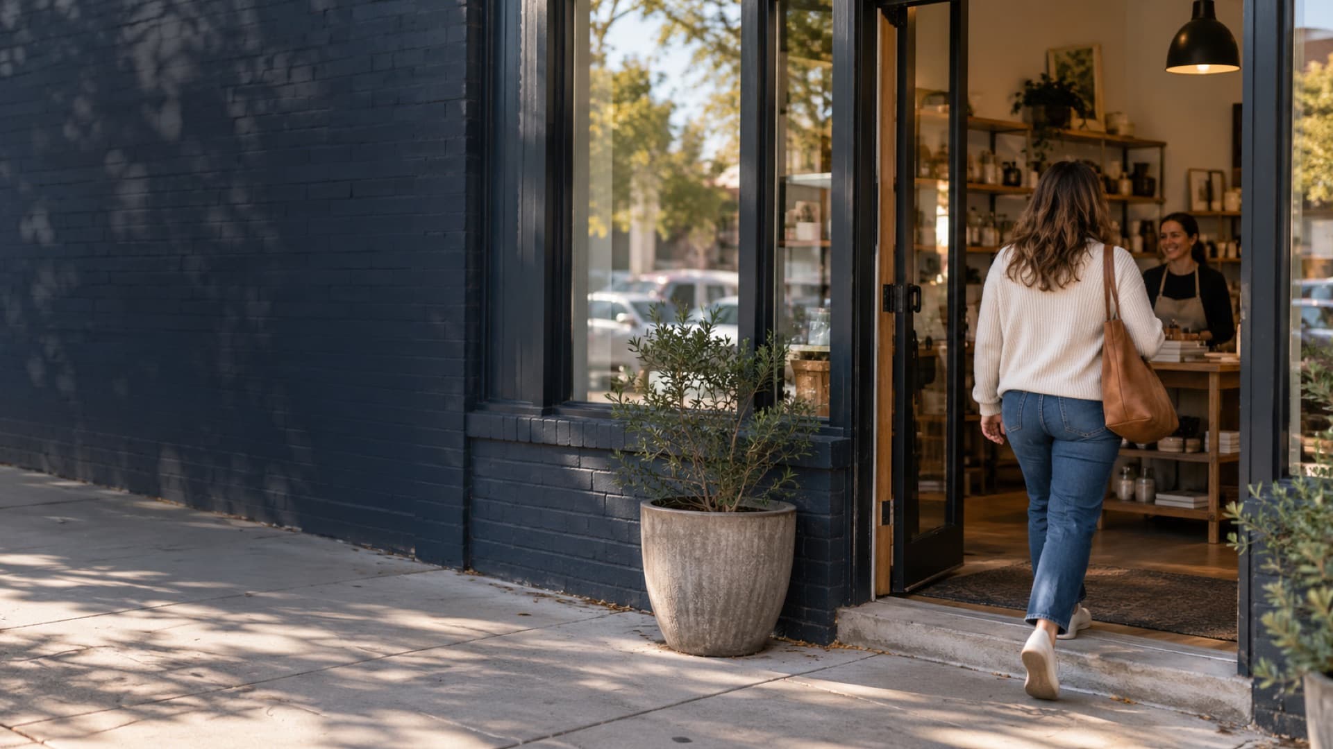 A customer walks through the open door of a local shop as the owner greets her
